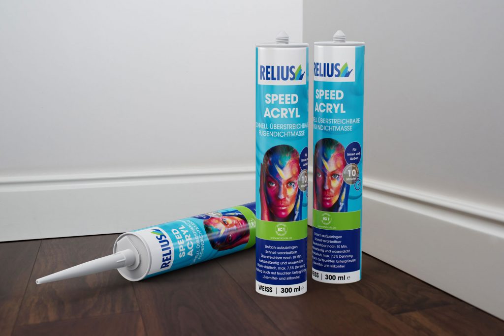 Drei Kartuschen Relius Speed Acryl als Stilleben vor weißer Fußleiste auf dunklem Holzboden, hybride Bildproduktion